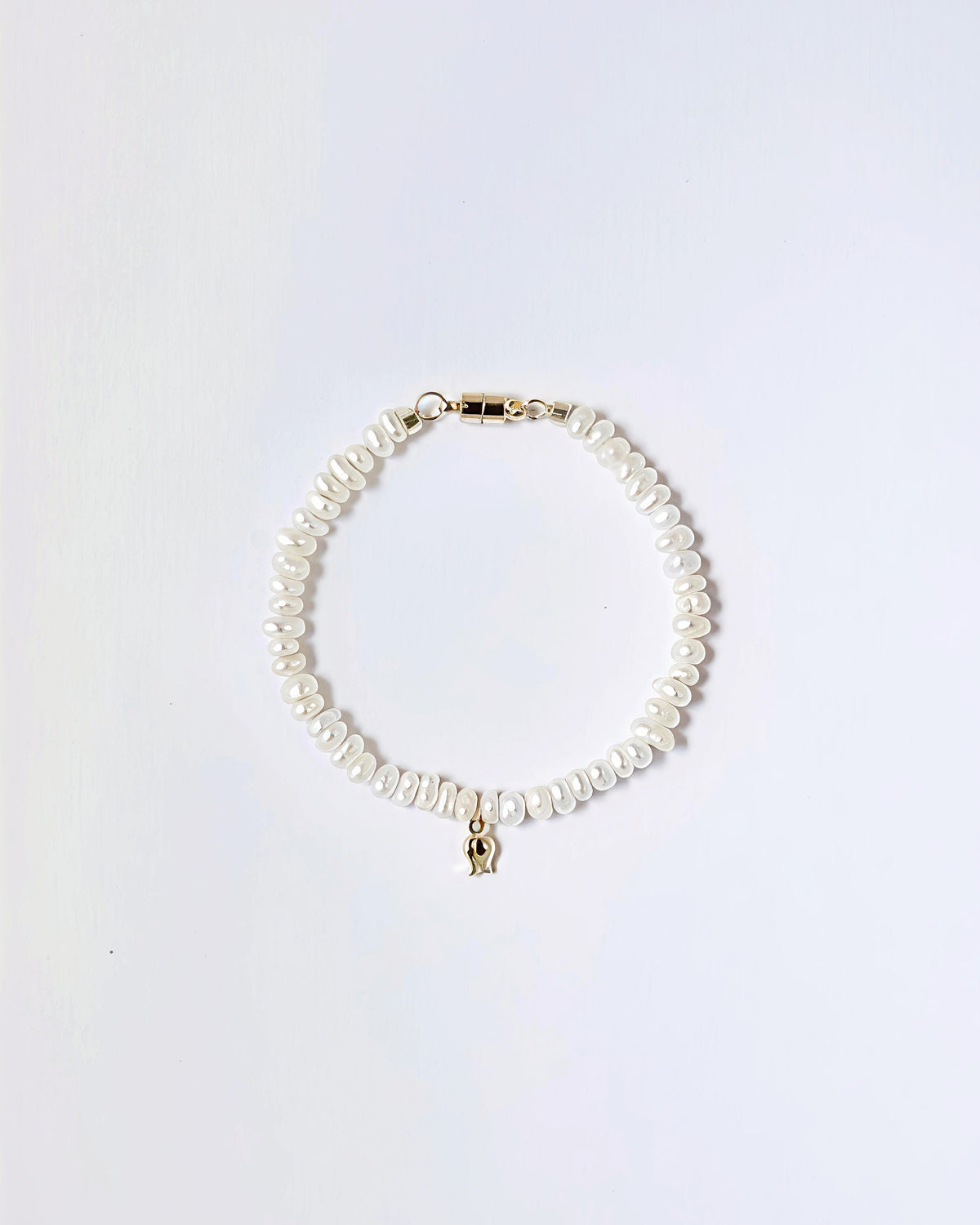 A delicate bracelet made of irregular white freshwater pearls with a small gold elephant charm and gold clasp, displayed on a clean white background.