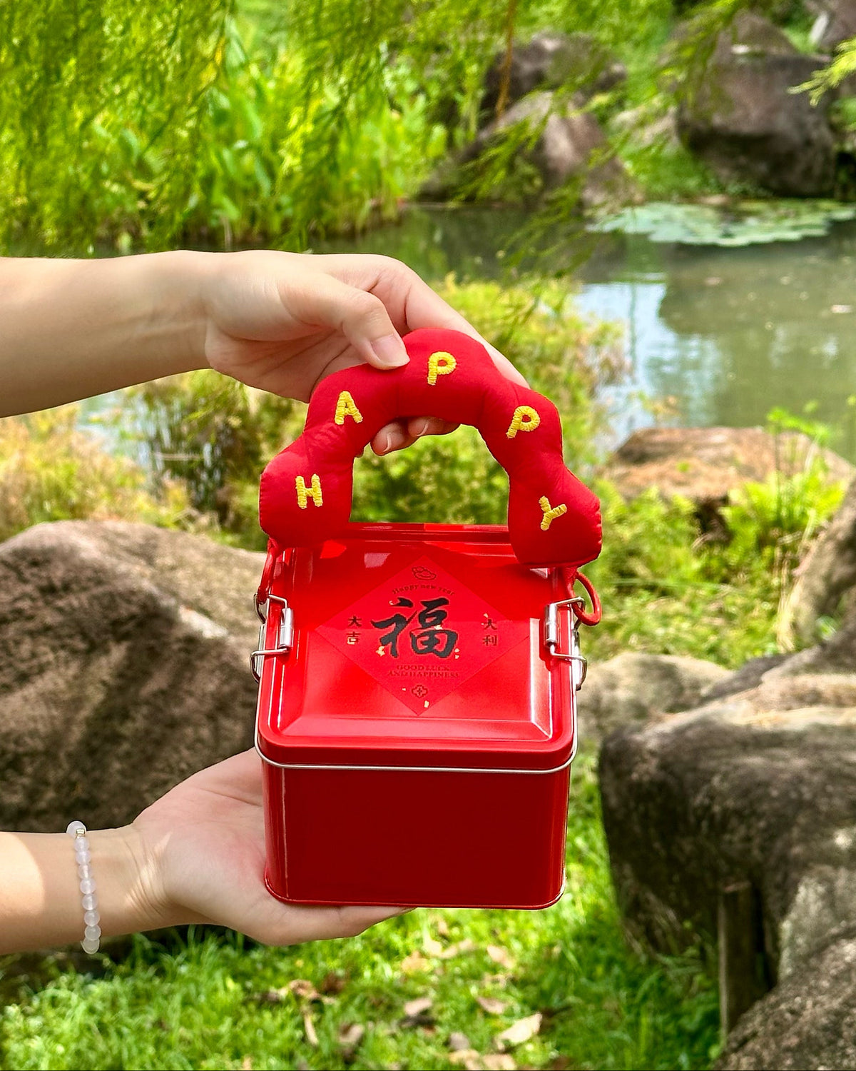 Red gift box symbolize prosperity with 'Happy' handle held by a hand in a natural setting