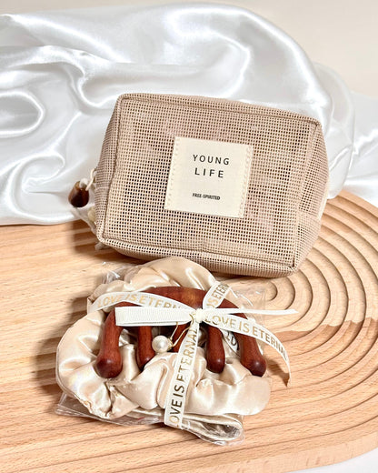 A champagne or beige mesh zip pouch with a cream label reading 'YOUNG LIFE' sits on a wooden board beside a satin scrunchie with wooden claw clips and a matching ribbon.